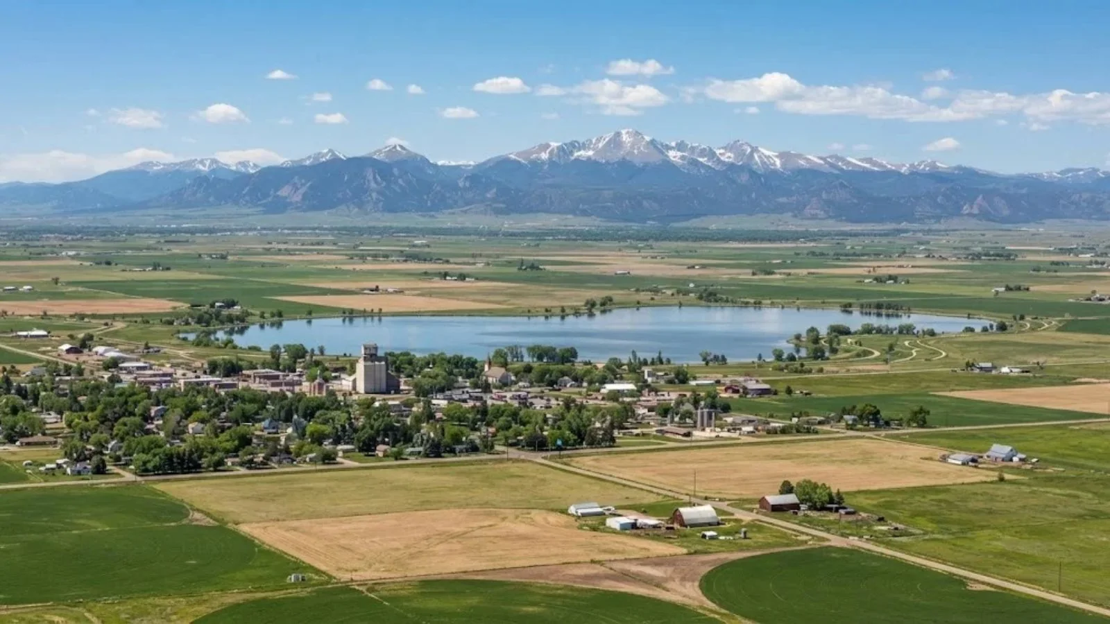 Aerial view of a town beside a lake with snow-capped mountains beyond farmland