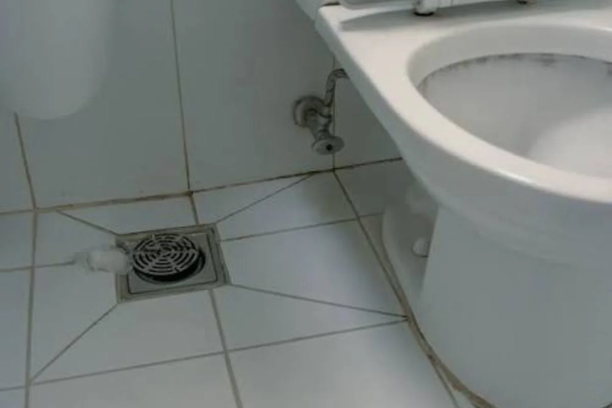 Floor drain on a tiled bathroom floor beside a toilet