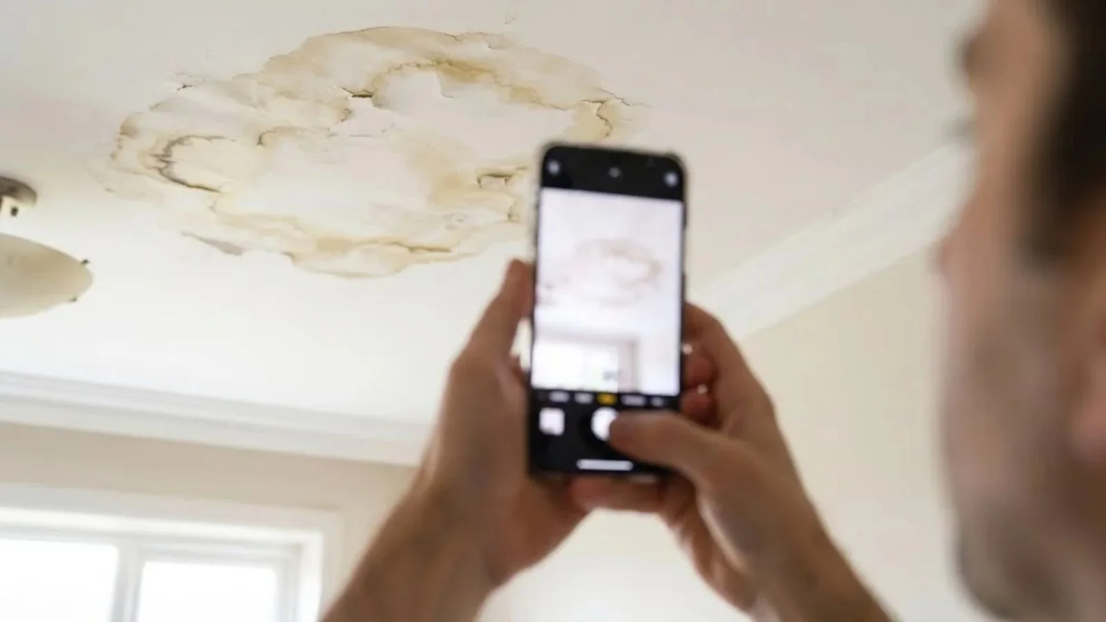 Hands holding a phone to photograph a water-stained ceiling