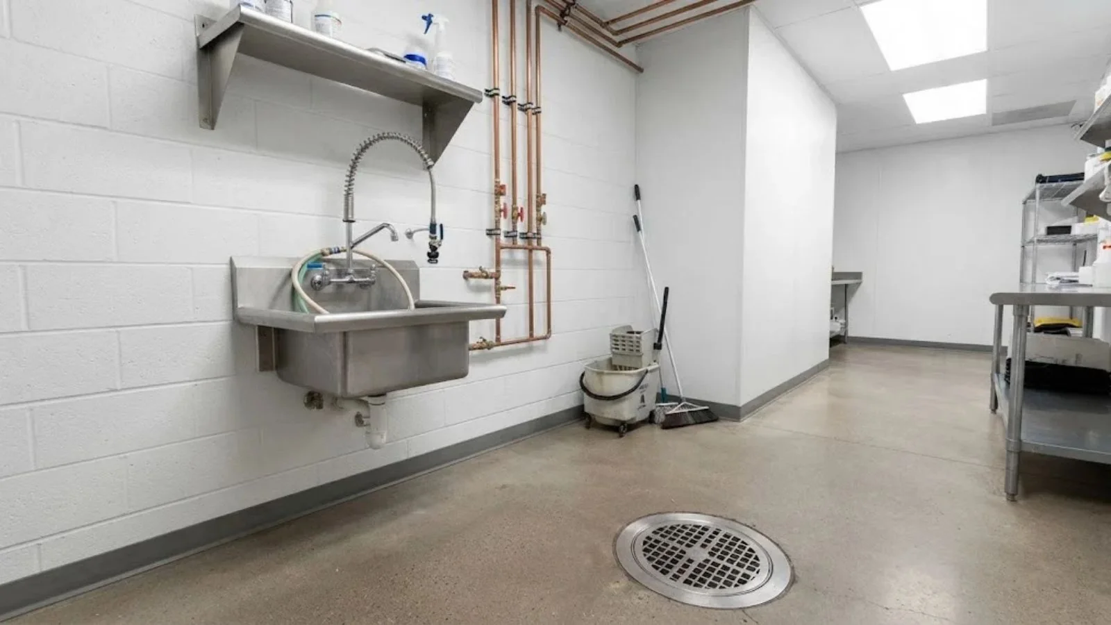 Back-of-house room with a stainless hand sink, a floor drain and exposed copper lines