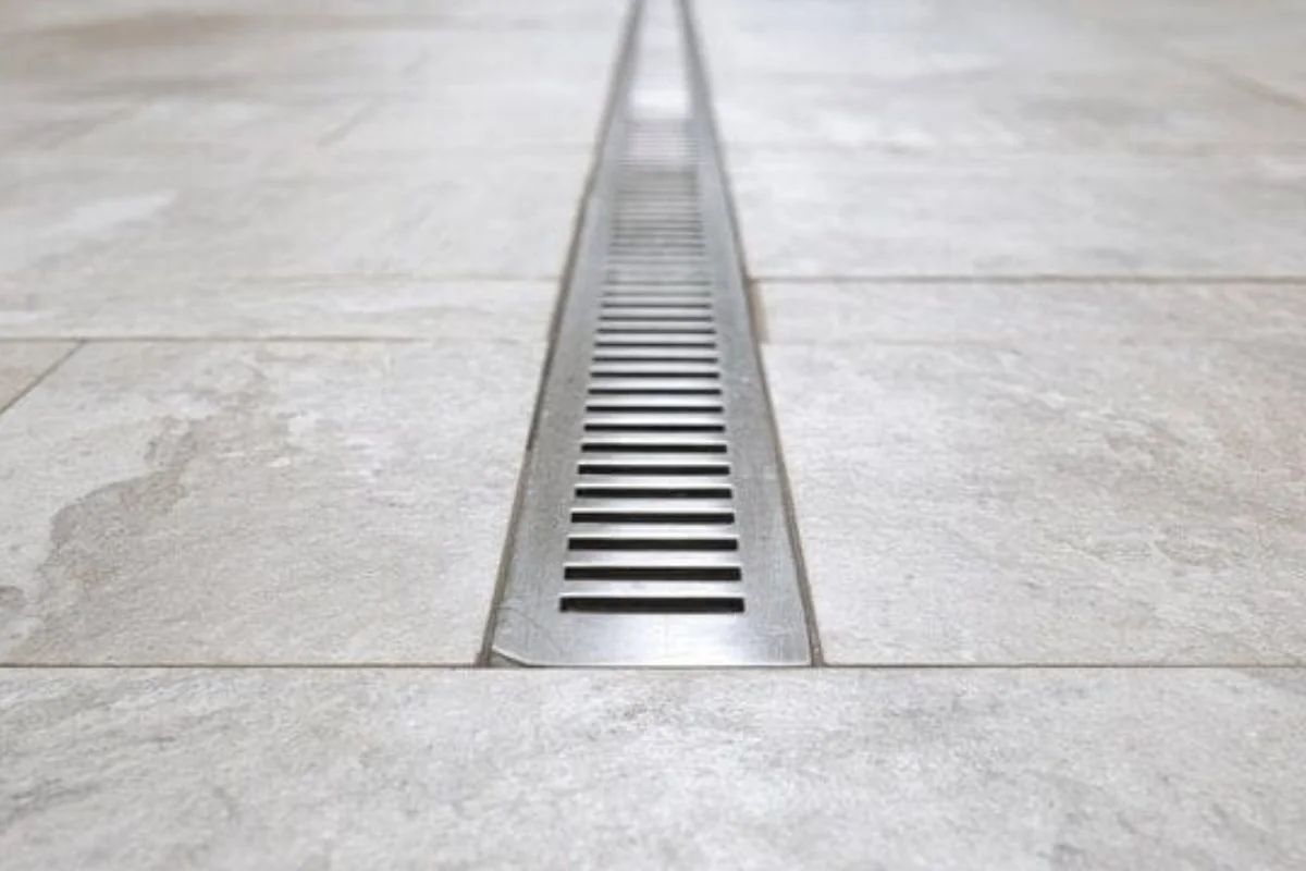 Stainless steel trench drain running across a tiled floor
