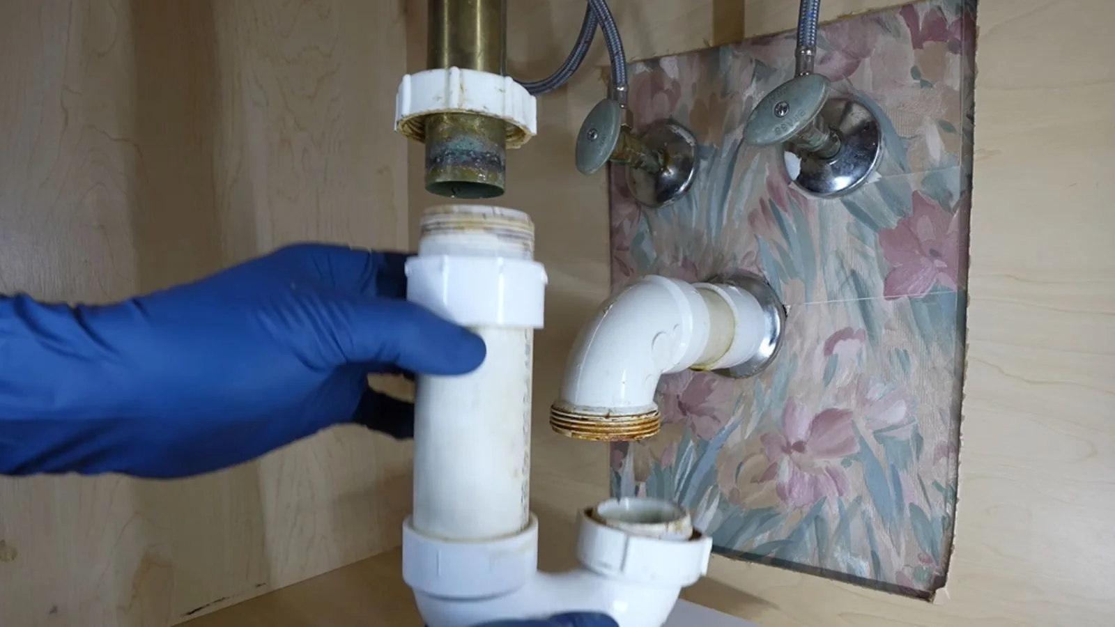 Gloved hand holding white drain piping under a sink