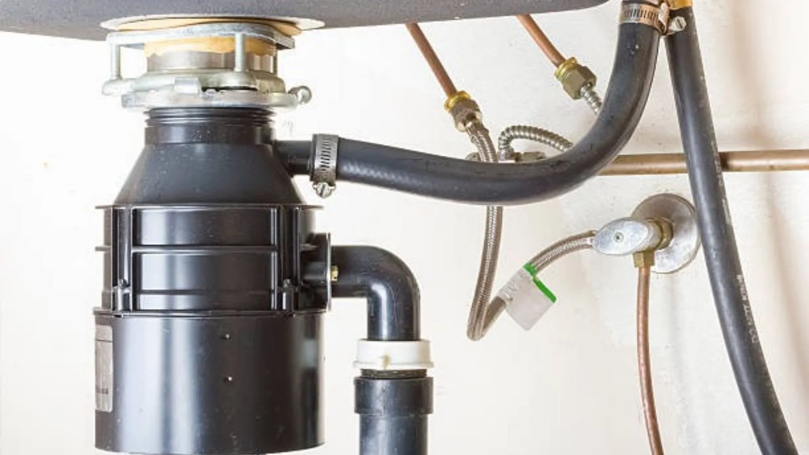 Garbage disposal mounted under a sink with supply lines and drain pipes