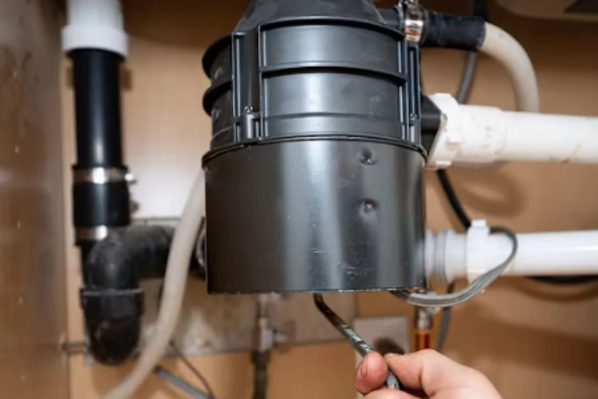Garbage disposal under a sink with a hand and tool reaching up from below