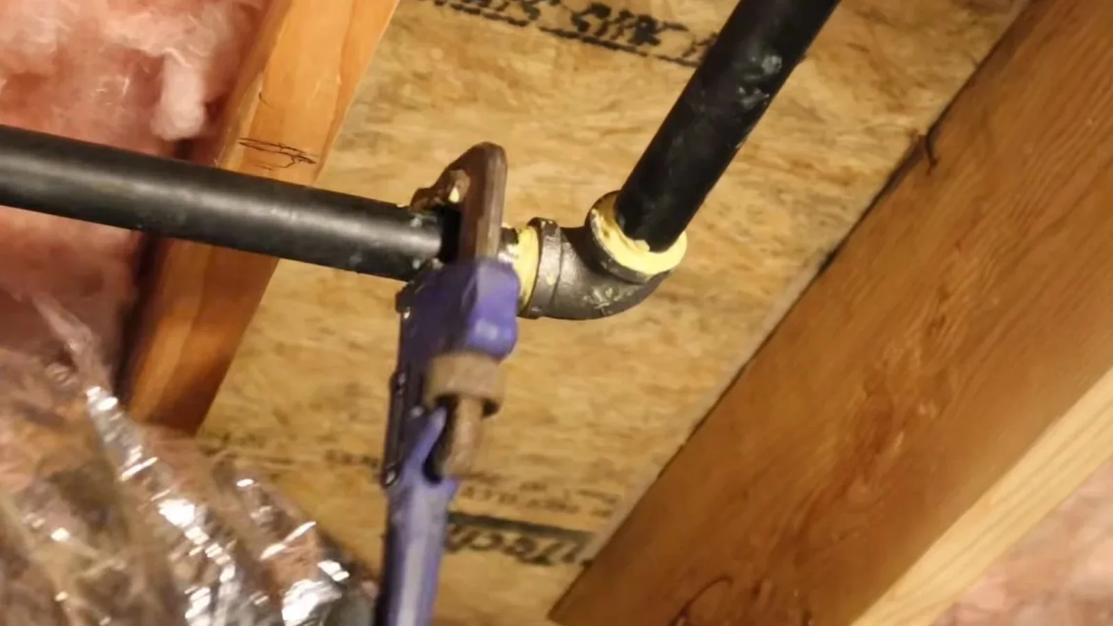 Black iron gas pipe with fittings running through an insulated joist space