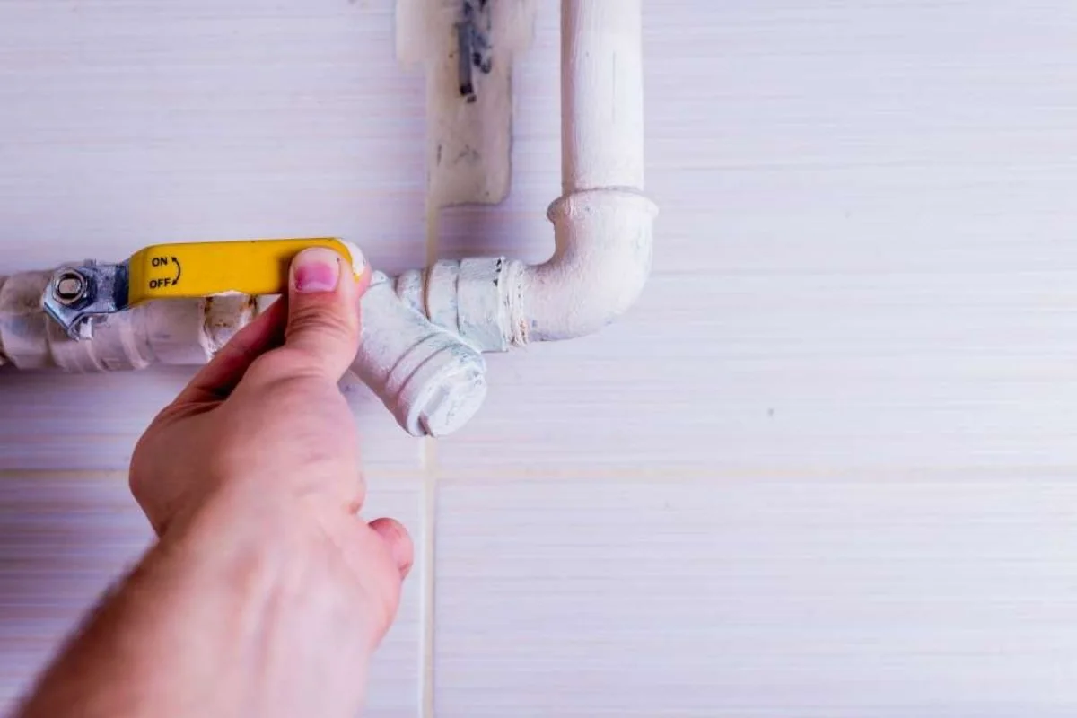 Hand on the yellow handle of a shutoff valve on a pipe