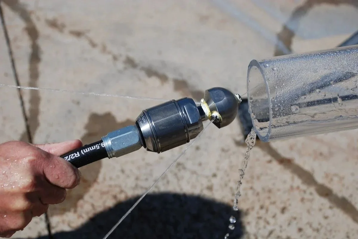 Multi-port jetting nozzle held in a hand with water dripping off a clear tube
