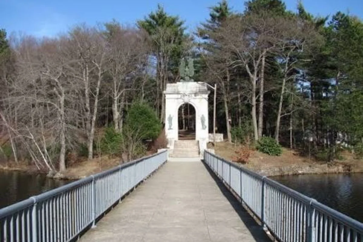 Footbridge over water leading to a white stone memorial arch