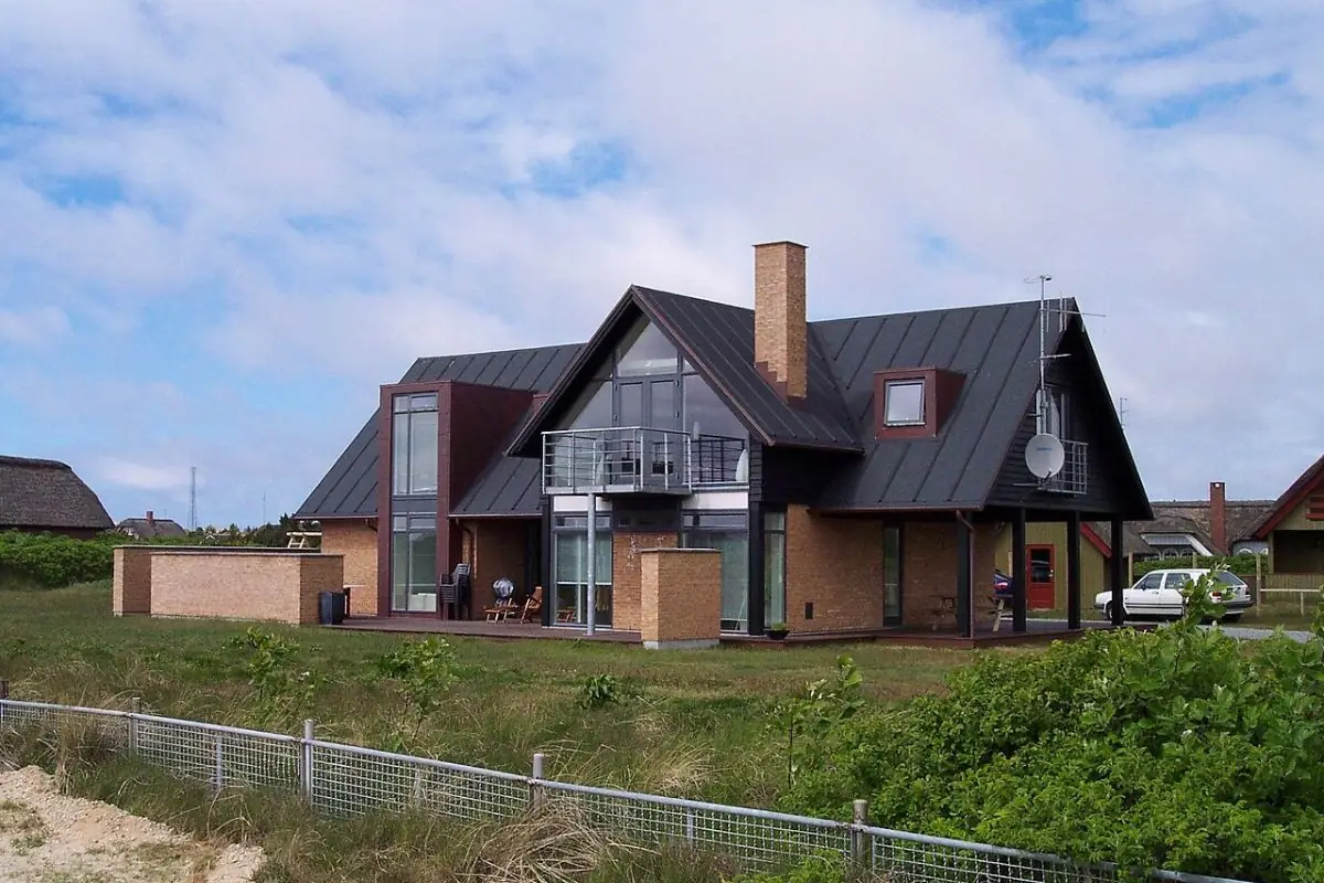 Dark-roofed modern house with large windows behind a low fence