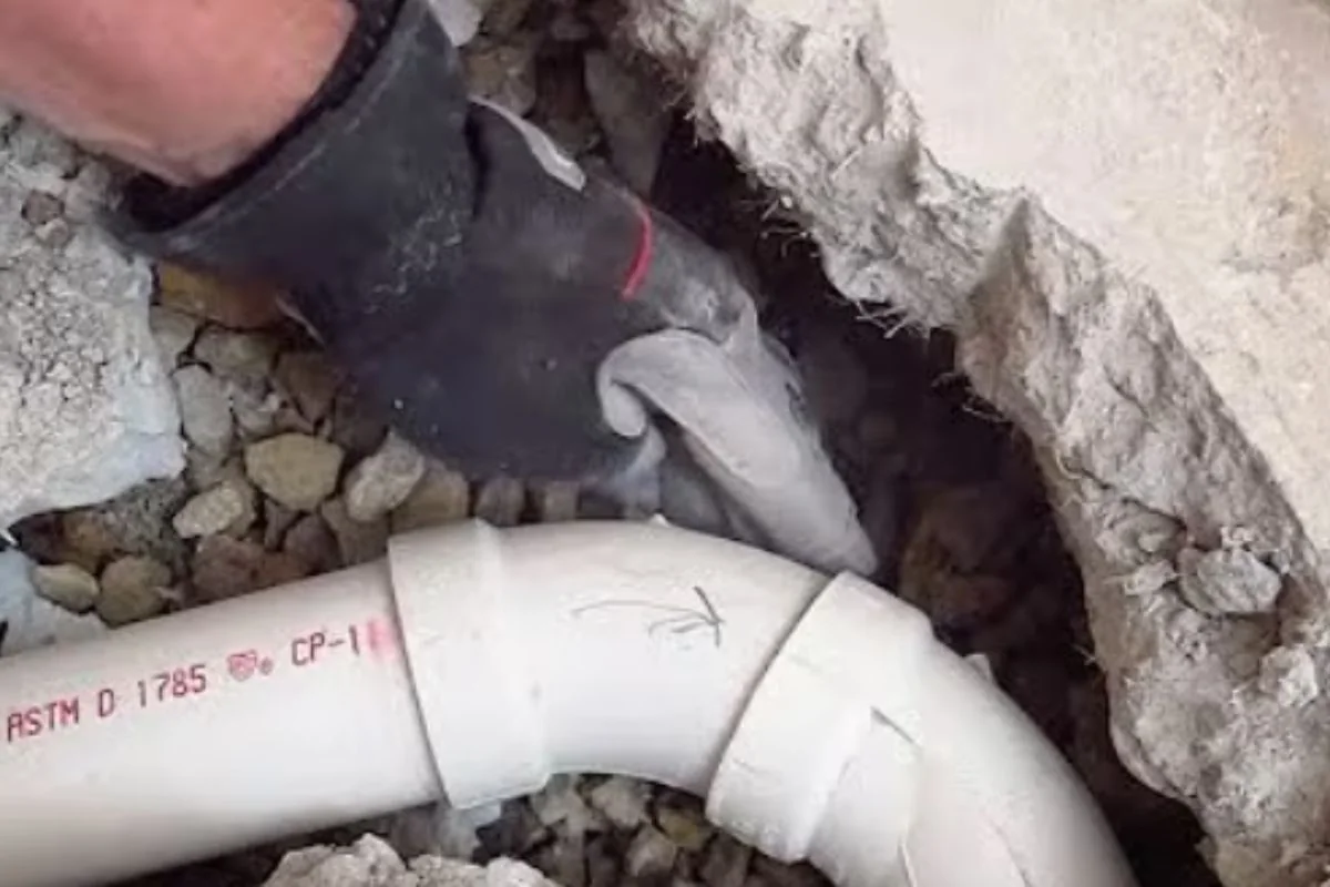 Gloved hand fitting white PVC sewer pipe in a trench with gravel