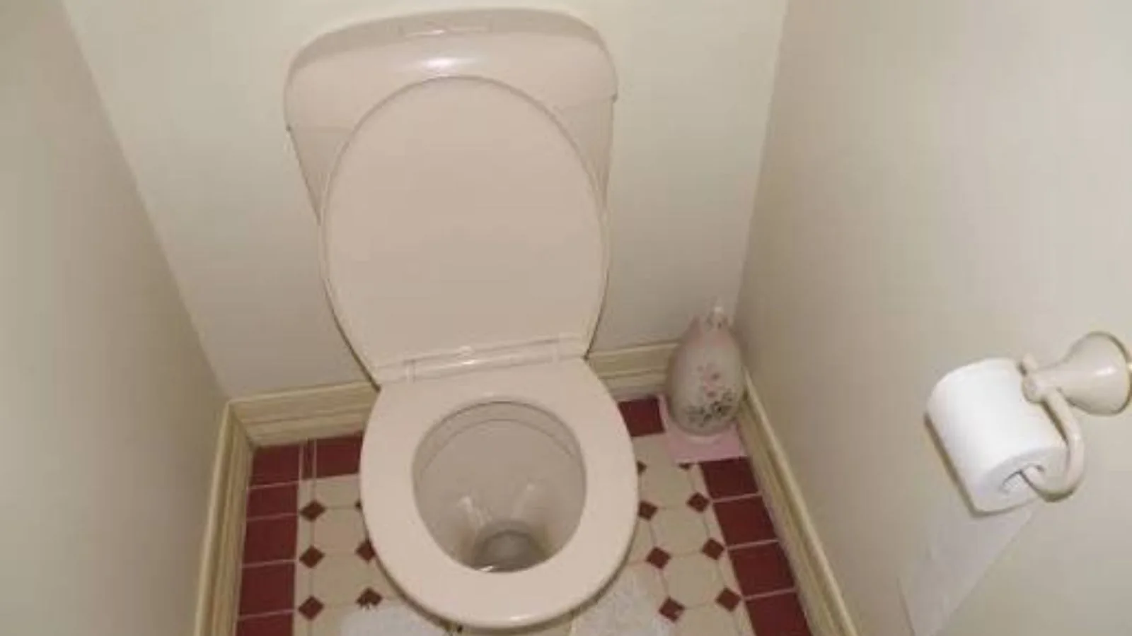Toilet in a small bathroom with a red and white tiled floor