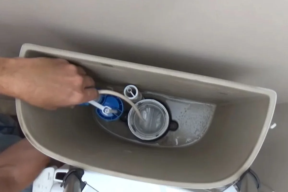 Hand adjusting the fill valve and flapper inside an open toilet tank
