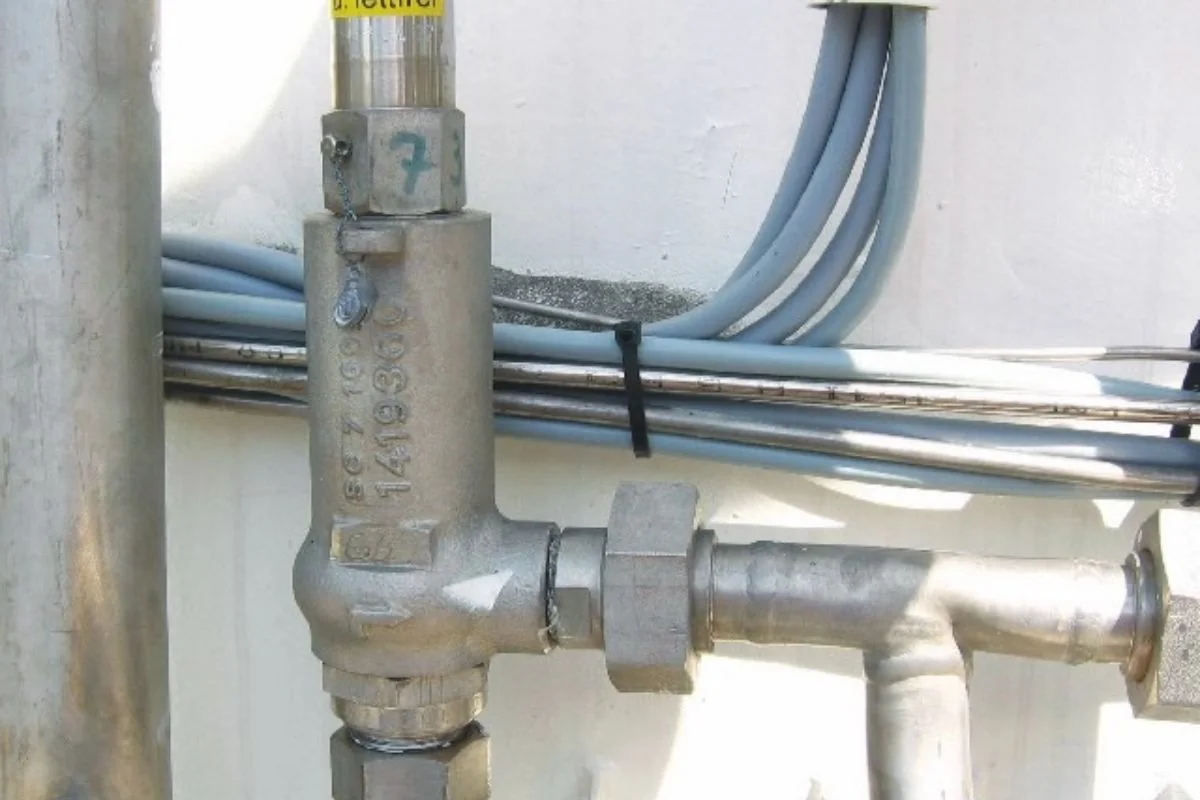 Metal pressure relief valve and pipework against a wall